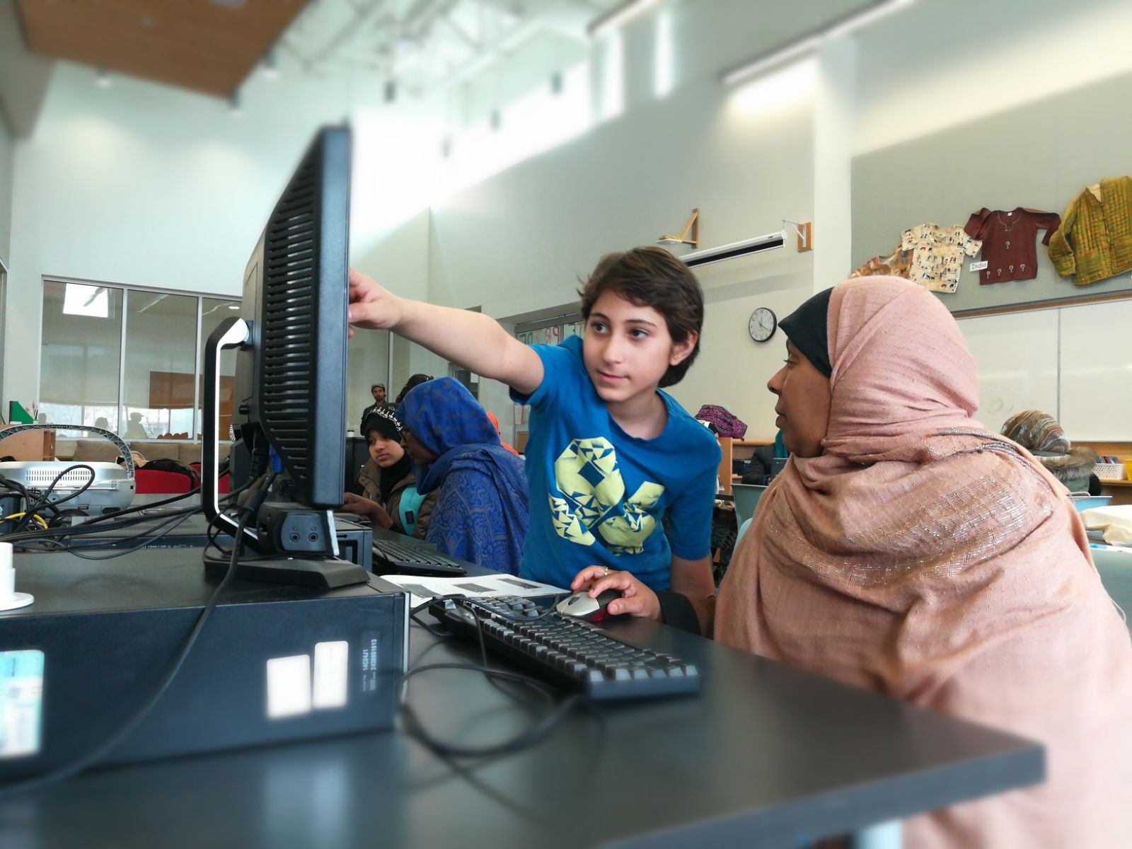 A young tutor pointing at a computer screen while the woman beside him uses the mouse