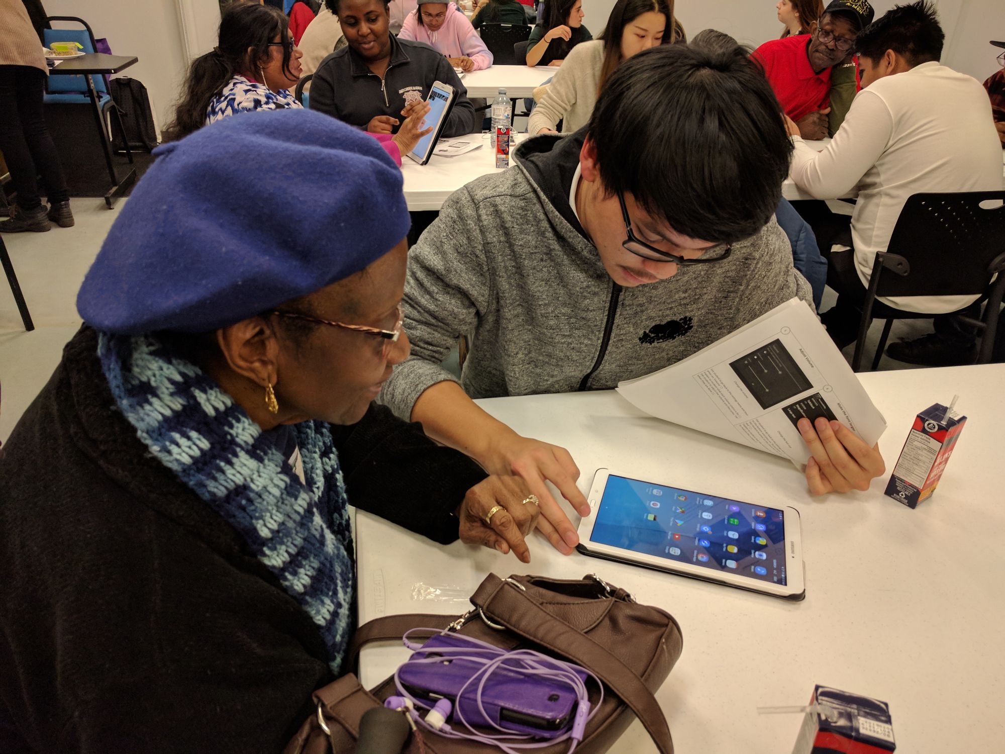 A youth tutor helping a senior learn on a tablet